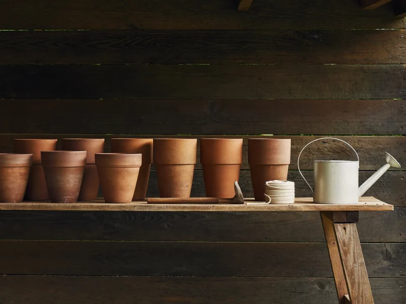Illustrative potting bench with clay pots, dibber, twine and a galvanised watering can